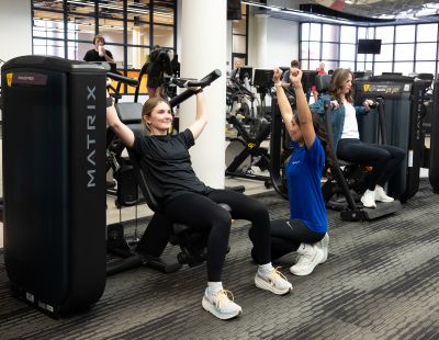 a woman engages in strength training in a gym setting with a personal trainer demonstrating