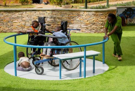 Children in wheelchairs are pushed on a spinner by an adult